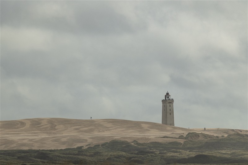 Ein Leuchtturm in einer Dünenlandschaft unter tiefen Wolken.